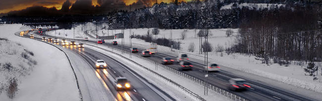 A photo showing vehicles driving on a snowing highway at dusk.