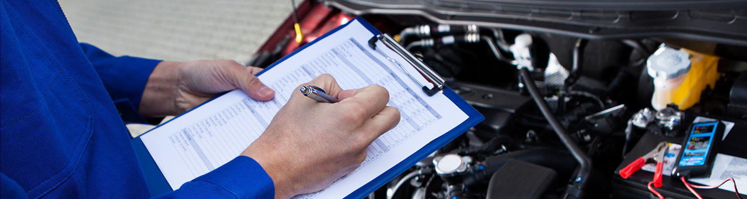 Photo showing a mechanic with a maintenance checklist looking over a vehicles engine compartment under a hood.